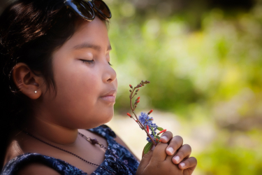 Hispanic little girl with her eyes closed and holding a bouquet of fresh wildflowers to her nose, enjoying the sweet fragrance of the plants.